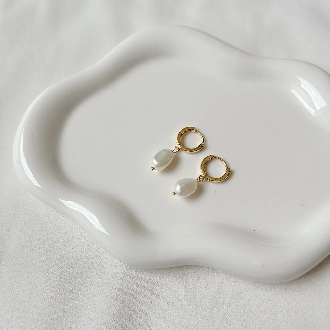Aros de perla con argolla dorada sobre una bandeja blanca